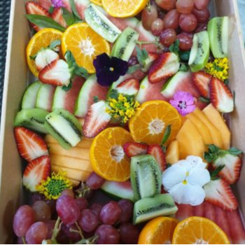Colourful fruit platter with sliced oranges, strawberries, kiwifruit, watermelon and grapes, garnished with edible flowers.